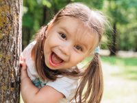 Close-up portrait of an excited little girl laughing in summer park